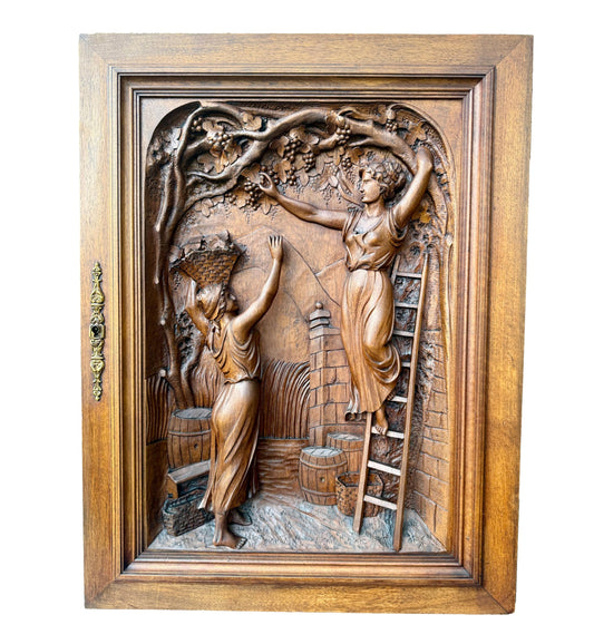 Antique 19th-century carved walnut door panel showing two women harvesting grapes in a vineyard, detailed French relief sculpture.