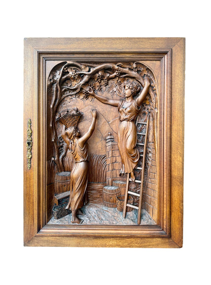 Antique 19th-century carved walnut door panel showing two women harvesting grapes in a vineyard, detailed French relief sculpture.