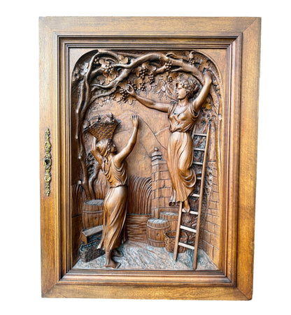 Antique 19th-century carved walnut door panel showing two women harvesting grapes in a vineyard, detailed French relief sculpture.