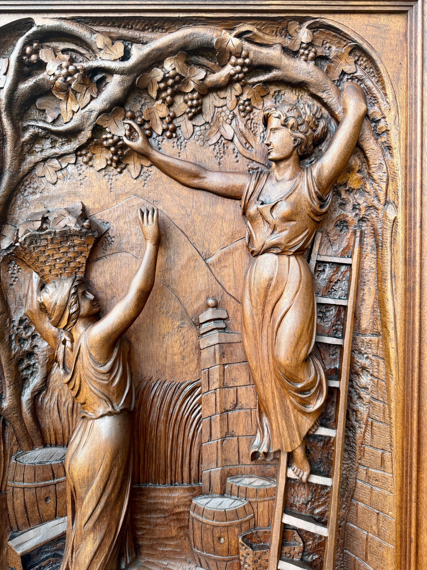 Antique 19th-century carved walnut door panel showing two women harvesting grapes in a vineyard, detailed French relief sculpture.