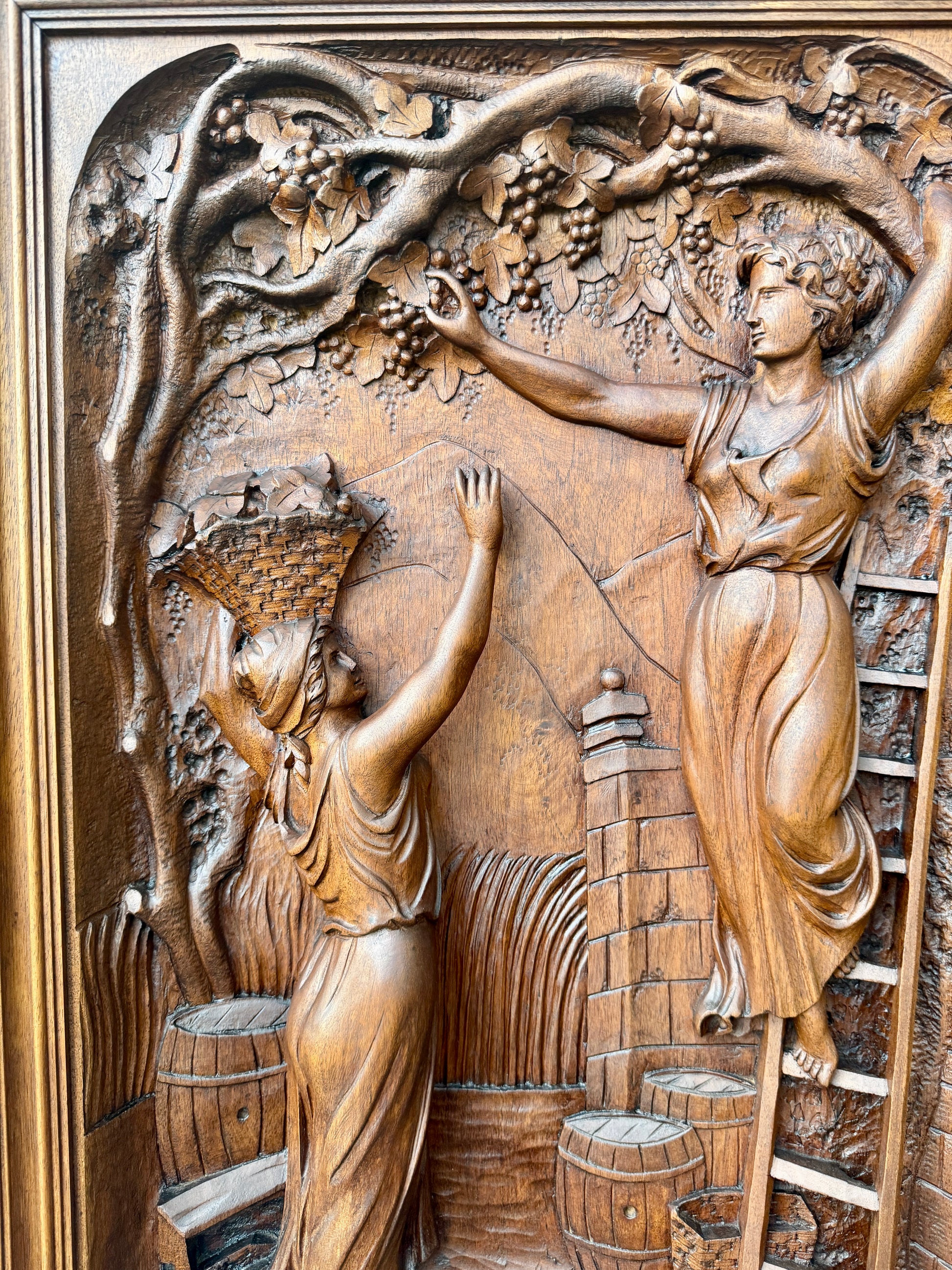 Antique 19th-century carved walnut door panel showing two women harvesting grapes in a vineyard, detailed French relief sculpture.